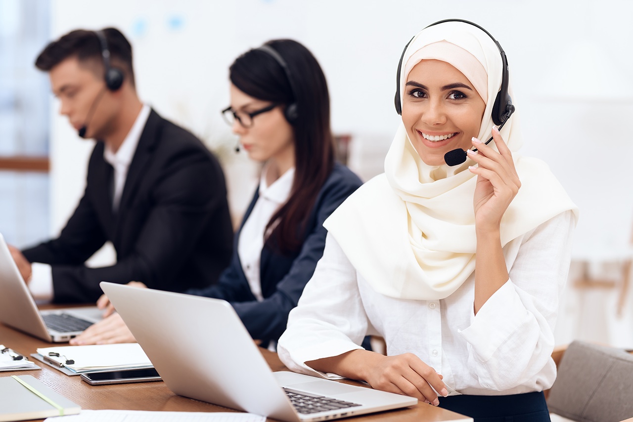 An Arab woman works in a call center. She's an operator. Her colleagues work nearby.