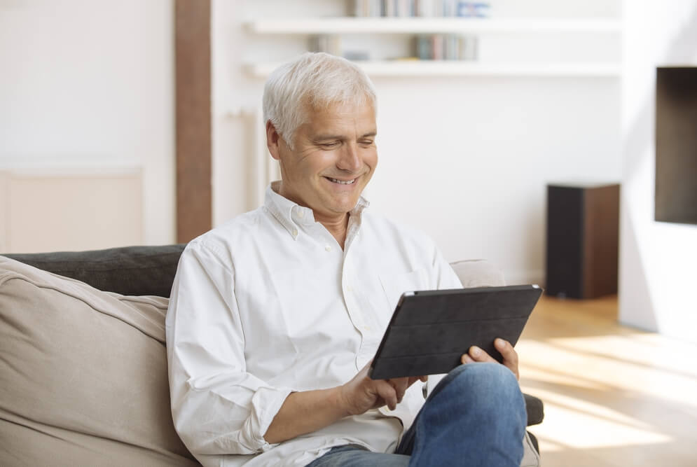 Smiling mature man sitting on a sofa using a tablet pc  in a living room; Shutterstock ID 651950971