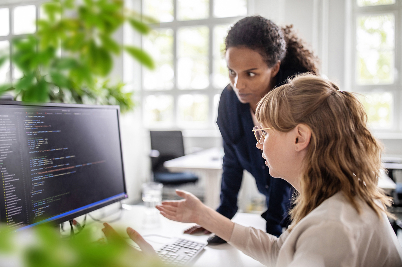 Businesswoman discussing with female coworker over coding on computer at desk in creative office
