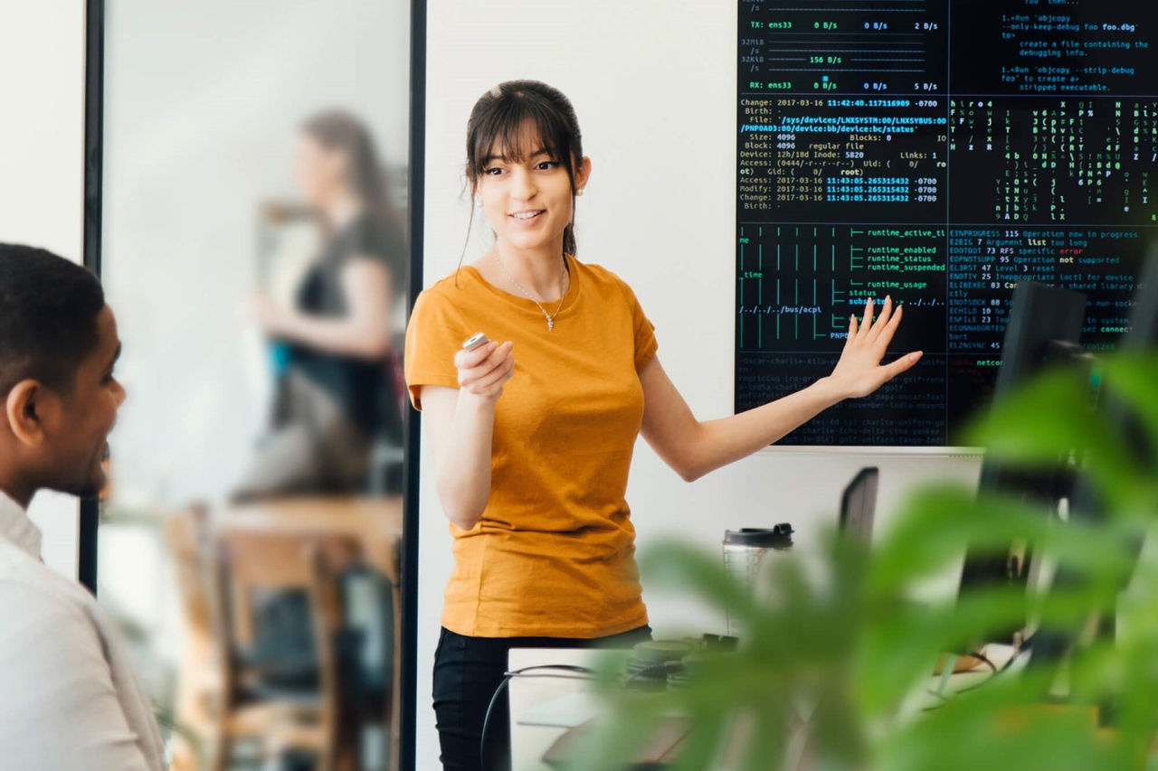 Businesswoman discussing with female coworker over coding on computer at desk in creative office