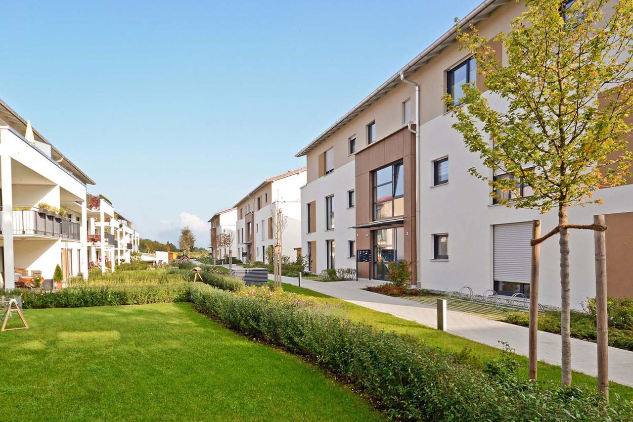 Lotissement moderne avec des immeubles d'habitation et beaucoup de pelouse ainsi que quelques arbres.