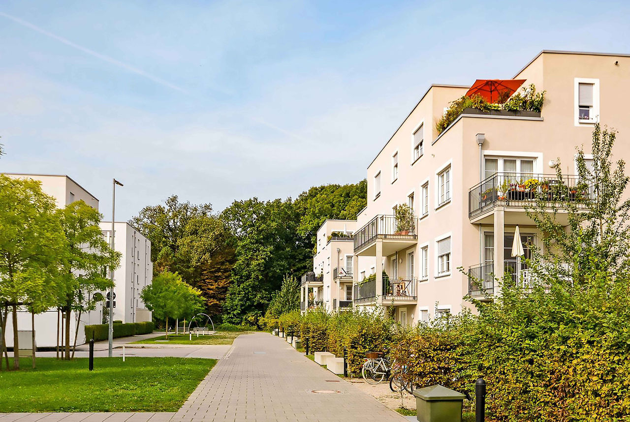 Immeuble d'habitation avec balcons, façades roses et plantes vertes sur fond de ciel bleu.