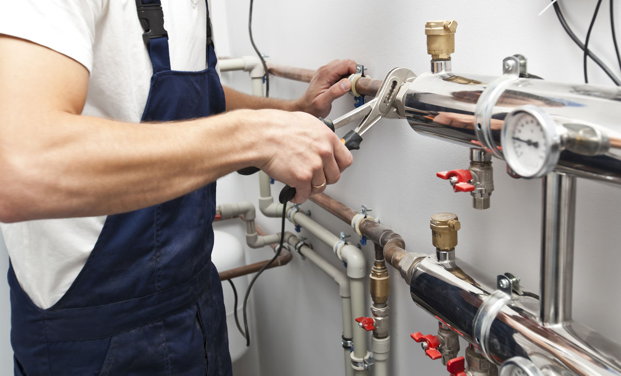 The man is installing the heater system in the house and checking pipes by the wrench