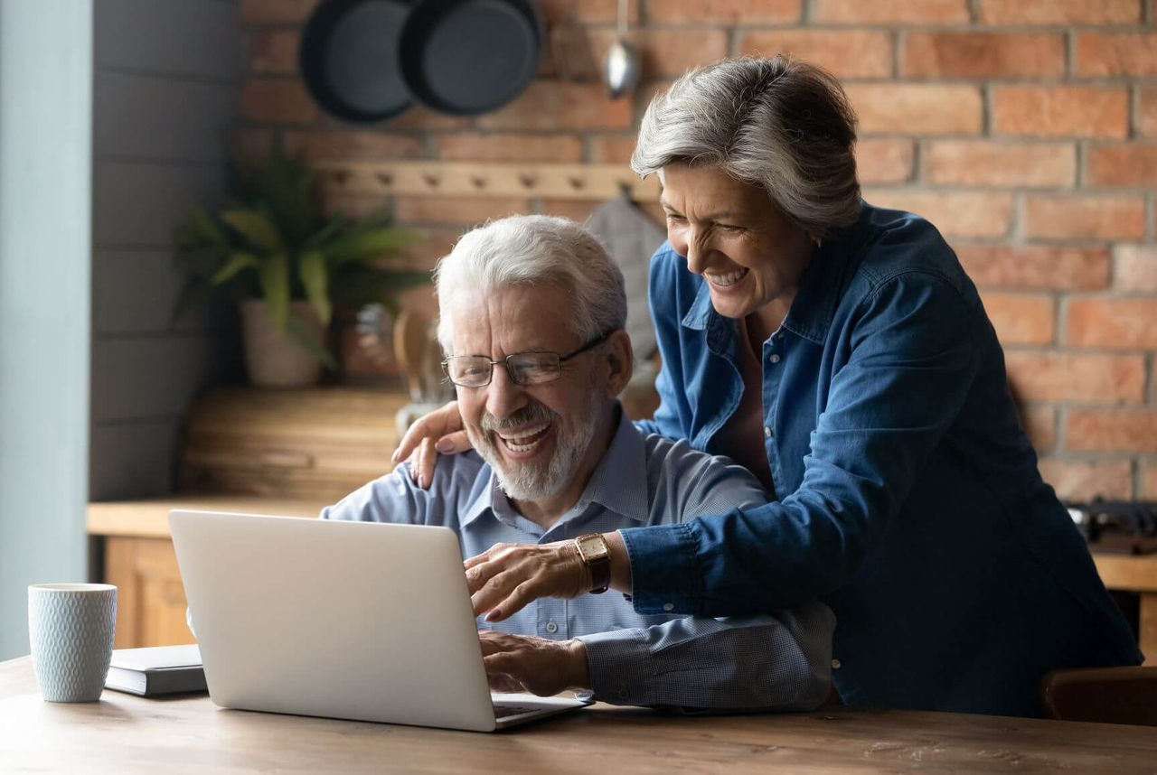 Ein lächelndes Ehepaar bedient einen Laptop und erstellt die Betriebskostenabrechnung.