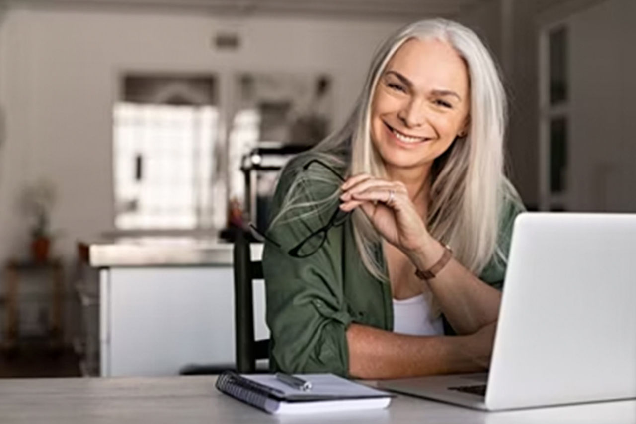 Kvinde sidder med bærbar computer i køkkenmiljø. 