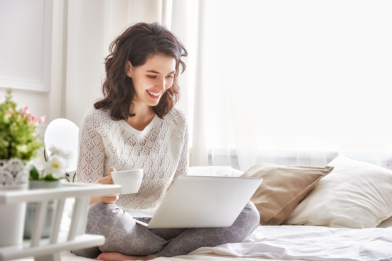 Happy casual beautiful woman working on a laptop sitting on the bed in the house.; Shutterstock ID 394104886