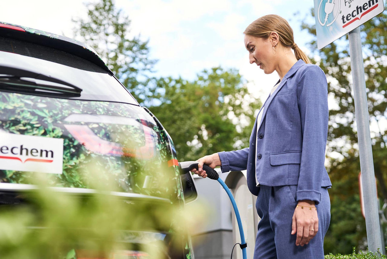 Une femme vêtue d'un costume en lin bleu charge une voiture électrique Techem.