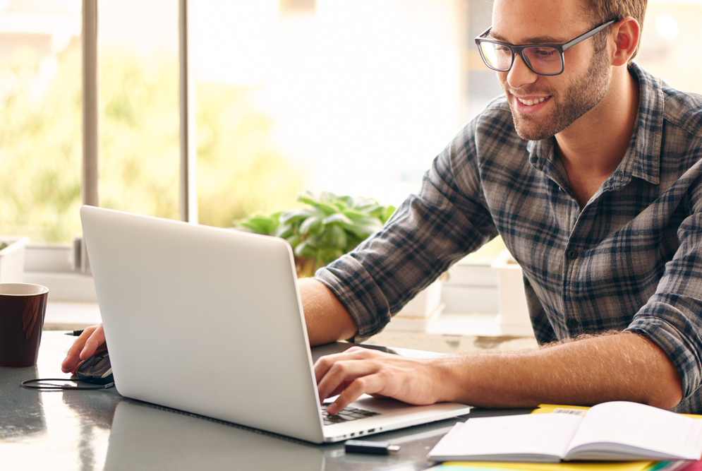 Happy young man, wearing glasses and smiling, as he works on his laptop to get all his business done early in the morning with his cup of coffee; Shutterstock ID 272163653